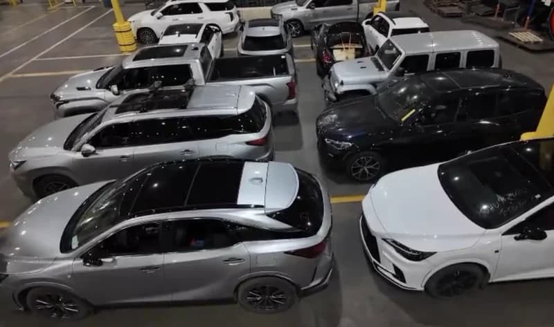 A high-angle photograph showing dozens of recovered luxury vehicles, including SUVs and sedans, parked closely together in an indoor warehouse facility. The image illustrates the significant scale of the international car theft ring recently dismantled by Ontario Police.