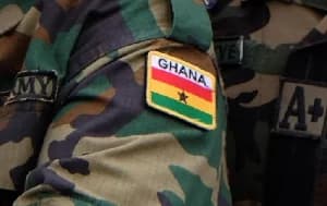 A close-up photograph showing the sleeve of a Ghana Army camouflage uniform. The sleeve features a prominent Ghanaian flag patch with the text 'GHANA' above it, alongside patches indicating 'ARMY' affiliation and blood type 'A+'.
