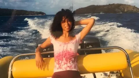 BBC Newsnight Lisa Phillips on a boat wearing a pink top and with her left arm posing behind her head. Epstein's island is in the background