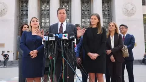 EPA/Shutterstock Mark Lanier wearing a dark pinstriped suit and patterned tie, standing in front of a bank of microphones and flanked by people either side of him.