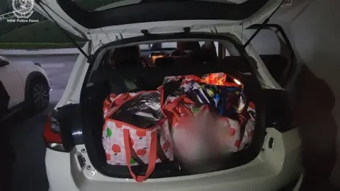 NSW Police Force Several red and white bags with apples on them in the boot of a white car.
