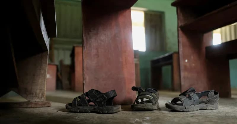 A low-angle photograph shows abandoned sandals on a dusty classroom floor amidst empty wooden desks. The scene evokes a sense of sudden disruption and loss, typical of reporting on school abductions in the region.