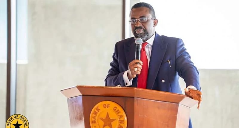 Maxwell Opoku-Afari, the First Deputy Governor of the Bank of Ghana, is captured speaking at a formal event from behind a wooden lectern. The podium prominently features the official seal of the Bank of Ghana, suggesting an official financial or regulatory address.