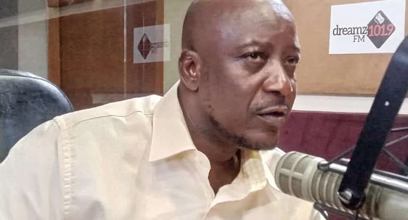 A close-up photograph of a man, identified as the Talensi District Chief Executive, speaking during a media engagement. He is captured in a radio studio setting with a professional microphone in the foreground and a Dreamz 101.9 FM logo on the wall behind him.