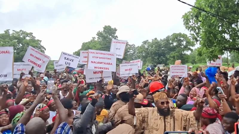 A large crowd of community members and workers in Gbani, Upper East Region, are seen holding up placards during a protest. The demonstrators are calling on the Minerals Commission and Earl International to respect court orders and protect the interests of Nalamtaaba Mining Enterprise. Many people are holding up smartphones to record the event, while signs display messages demanding an end to shooting and adherence to the law.