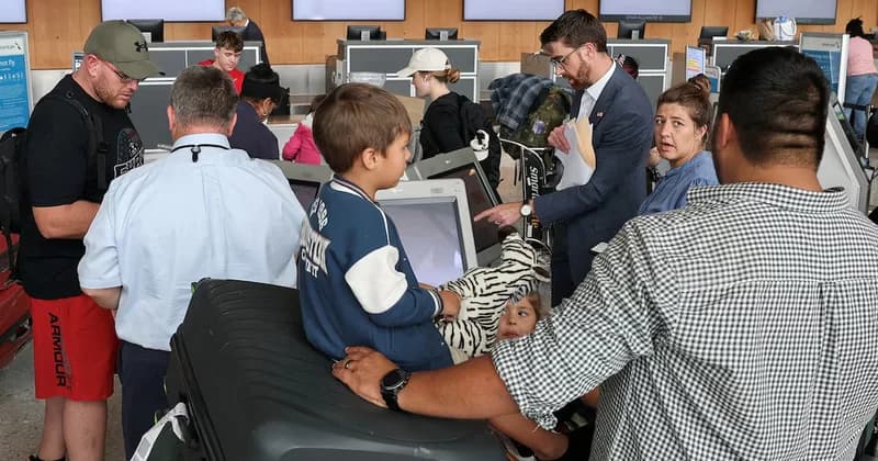 A group of travelers, including young children and adults, are gathered at an airport check-in or processing area. A man in a business suit is seen holding documents and pointing at a self-service kiosk screen while others manage luggage and wait in line.