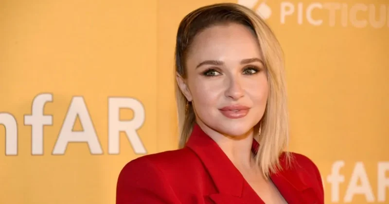 A headshot of actress Hayden Panettiere posing against a bright yellow background at a formal event. She is wearing a vibrant red blazer and her hair is styled in a sleek blonde bob.