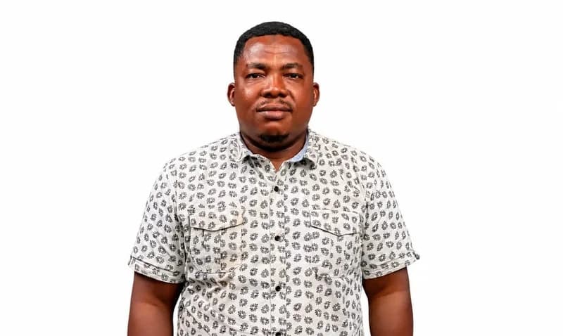A head-and-shoulders portrait of a man, likely a representative of the Positive Action Group (PAG), wearing a patterned grey and black short-sleeved shirt. He is posed against a plain white background, looking directly at the camera with a neutral expression.