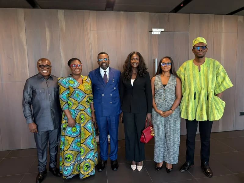 A group of six officials from the Ghana TVET Service and the Bank of Ghana standing together for a commemorative photo during a courtesy call. They are dressed in a mix of formal suits and vibrant traditional Ghanaian attire, including a green smock and a patterned kaba and slit, set against a modern wood-paneled background.