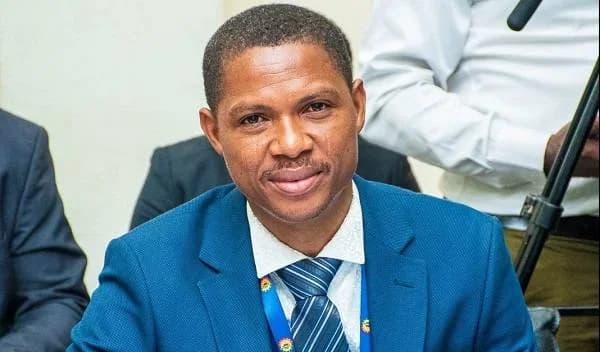 A close-up photograph of Francis-Xavier Sosu, the Member of Parliament for Madina, wearing a sharp blue suit, a white shirt, and a blue striped tie. He is looking directly at the camera in a formal setting, with parts of other people visible in the blurred background.