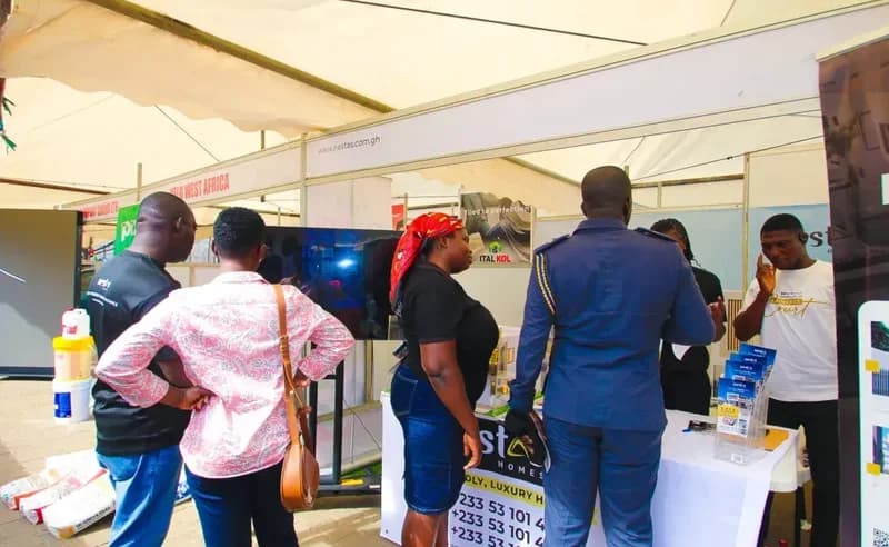 Attendees at the Republic Bank-JoyNews Habitat Fair Clinic interact with exhibitors at a booth for Nestas Homes. The photograph shows various visitors inquiring about real estate options and construction products such as paint and tiling under a large event marquee.