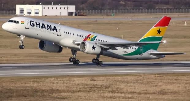 A Ghana International Airlines Boeing aircraft is captured during takeoff from a runway. The plane prominently displays the Ghanaian national colors—red, gold, and green—on its tail fin and engines, along with the black star symbol.
