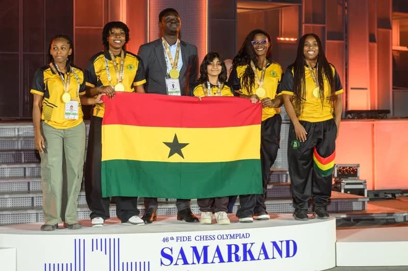Members of the Ghana National Chess Team, known as The Golden Knights, pose on a victory podium at the 46th FIDE Chess Olympiad in Samarkand. The group is seen holding the Ghanaian national flag and wearing gold medals following their successful participation in the international tournament.