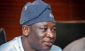 A close-up portrait of Samuel Nartey George, a prominent Ghanaian politician and Member of Parliament. He is seen wearing a traditional blue and white striped smock cap, looking attentively off-camera. He currently serves as the Chairman of the Communications Committee in Parliament, making him central to the article's topic.