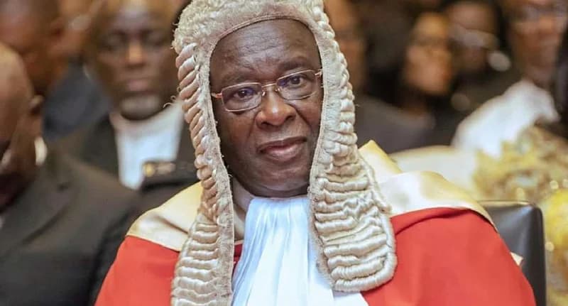 A close-up photograph of a high-ranking Ghanaian judicial officer, wearing a traditional ceremonial white peruke (wig) and scarlet robes. The official is seen wearing spectacles and a white bib, representing the formal attire of the Superior Courts of Ghana.