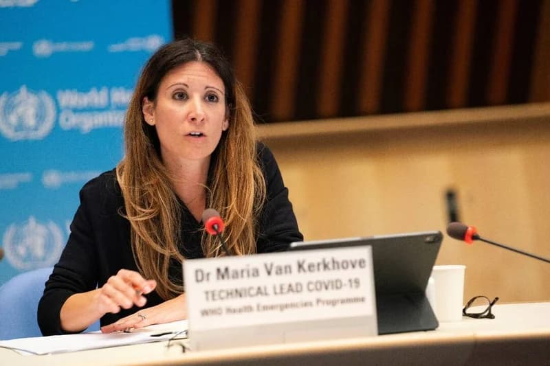 Dr. Maria Van Kerkhove, a prominent official at the World Health Organization, is pictured speaking during a formal health briefing. She is seated behind a nameplate that identifies her as the Technical Lead for COVID-19 within the WHO Health Emergencies Programme, with microphones and digital devices on the desk.