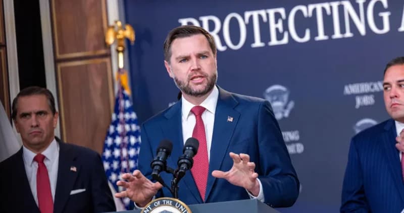 U.S. Vice President J.D. Vance speaks at a podium during a government briefing focused on domestic labor policy. He is flanked by two associates in suits, standing before a backdrop that reads 'PROTECTING AMERICAN JOBS'.