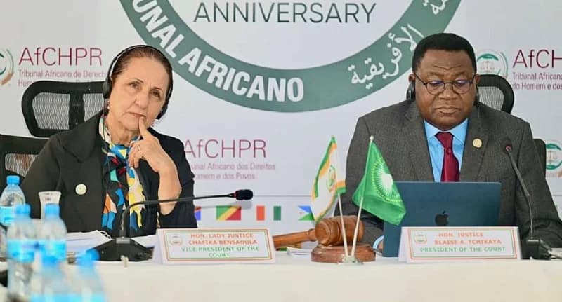 Hon. Justice Blaise A. Tchikaya, President of the African Court, and Hon. Lady Justice Chafika Bensaoula, Vice President, are pictured presiding over an official session of the African Court on Human and Peoples' Rights. The setting includes formal nameplates, microphones, a gavel, and an African Union flag, with an anniversary backdrop behind them.