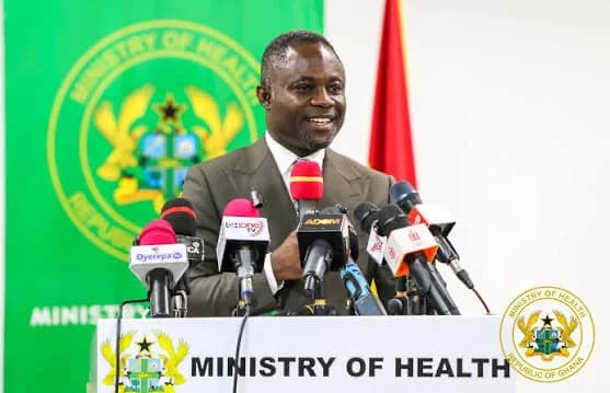 Dr. Bernard Okoe Boye, the Minister of Health, addresses the media during a press conference in Ghana. He stands behind a white podium featuring the Ministry of Health logo and 'REPUBLIC OF GHANA' text, with multiple media microphones positioned in front of him.