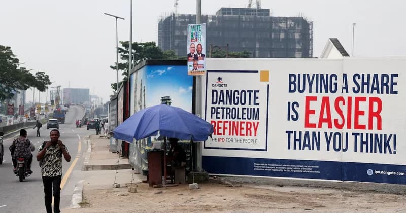 A large billboard for the Dangote Petroleum Refinery IPO is displayed prominently alongside a busy city street. The advertisement features the slogan 'BUYING A SHARE IS EASIER THAN YOU THINK!' while pedestrians and traffic move past in the foreground and background.