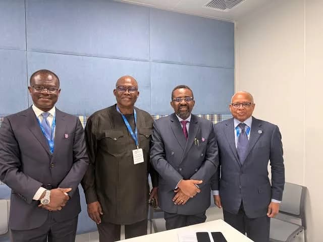 Four Ghanaian officials, including Finance Minister Dr. Mohammed Amin Adam and Bank of Ghana Governor Dr. Ernest Addison, stand together in a formal indoor setting. The men are dressed in professional attire and wearing identification lanyards, suggesting they are attending an international conference or summit.