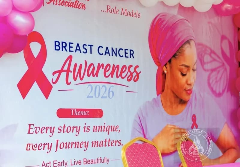 A promotional banner for a breast cancer awareness campaign in Ghana, featuring a woman in a pink headwrap and the classic pink ribbon logo. The display includes the 2026 awareness theme 'Every story is unique, every Journey matters' and is decorated with pink balloons and chairs.