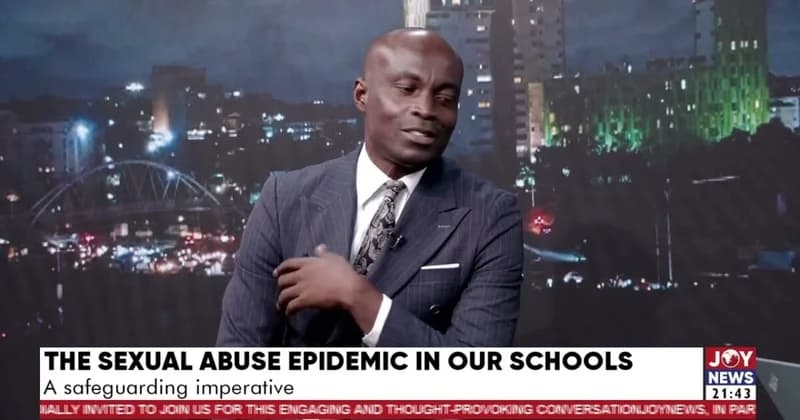 A man in a pinstripe suit and patterned tie speaks during a televised news segment on Joy News. The program's lower third title reads 'THE SEXUAL ABUSE EPIDEMIC IN OUR SCHOOLS' against a backdrop of a city skyline at night featuring a prominent bridge.